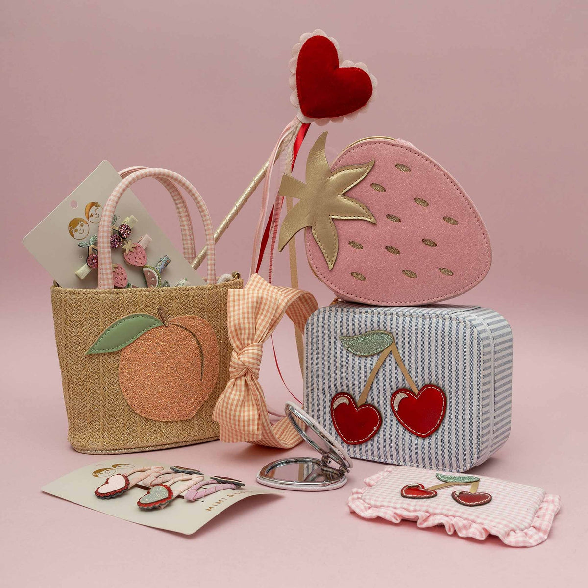 Set of children's accessories including a small bag, mirror, and heart-shaped items on a pink background