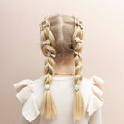 Back view of a child with blonde hair styled in braids, wearing a white top with ruffled sleeves on a beige background.