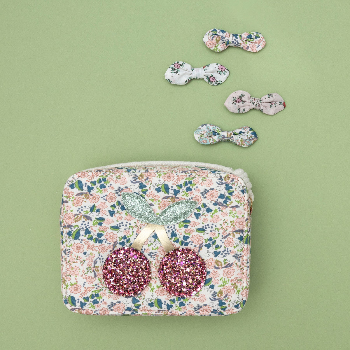 Four floral bow hair clips and floral pouch bag on a green background