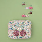 Floral patterned pouch with pink glittery earrings and decorative hair clips on a green background