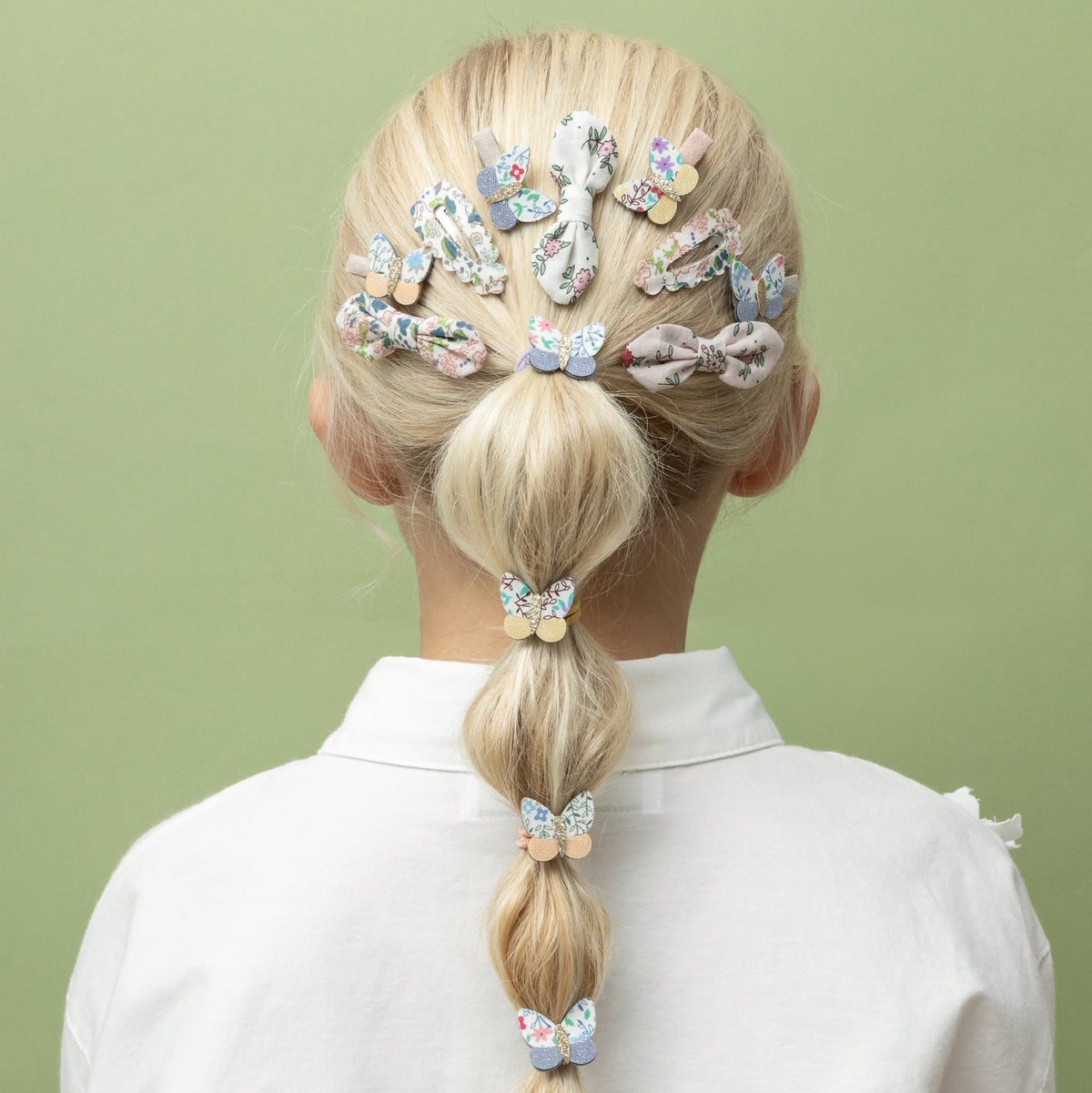 Person with a braid wearing colorful hair clips on a green background