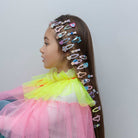 Child with colorful hair clips in a ponytail against a plain background
