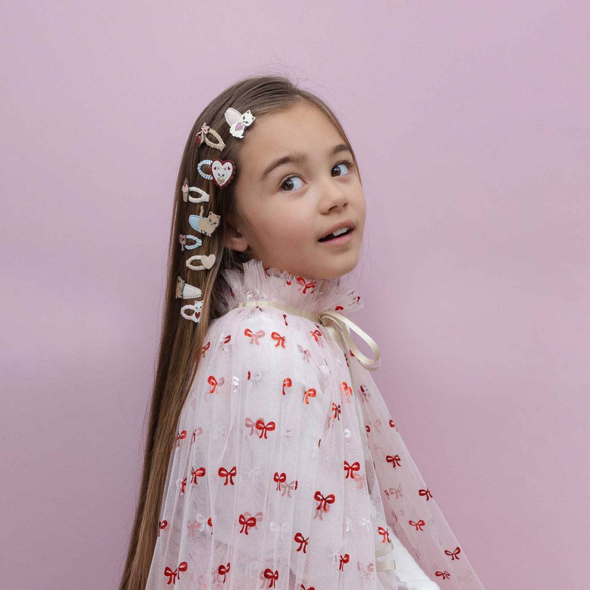 Young girl with decorative hair clips against a pink background