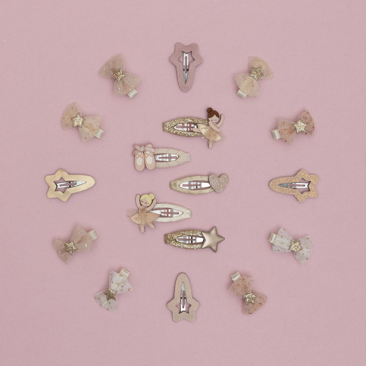 A set of 16 pastel hair clips arranged in a circle on a solid pink background. The clips feature whimsical designs including fairies, ballerinas, stars, bows, and hearts in soft pink, beige, and white tones with glittery and metallic details.