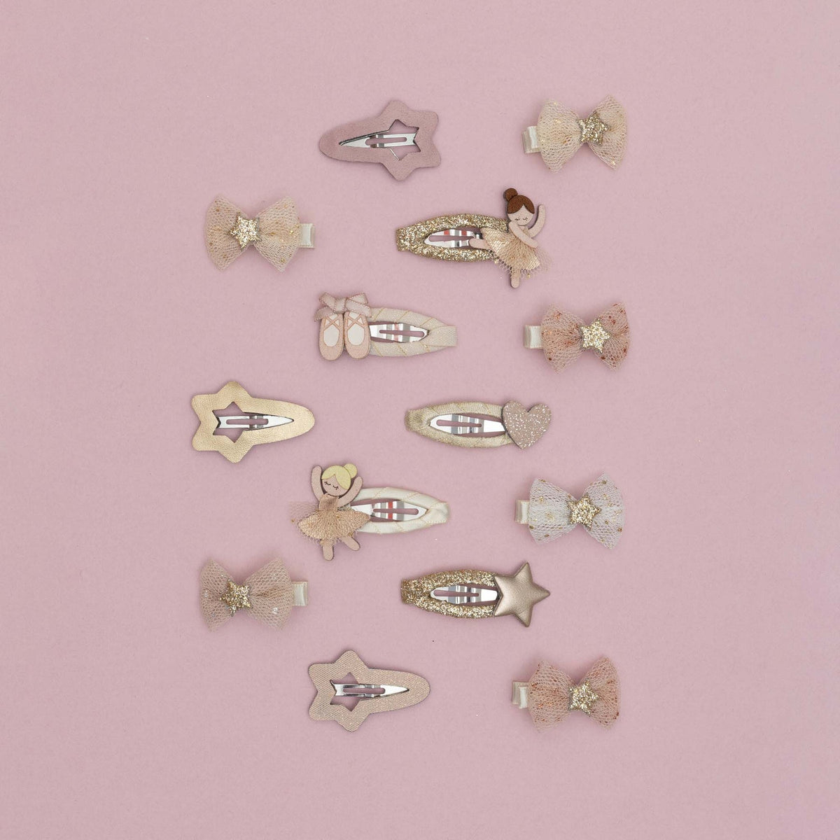 A set of 12 pastel hair clips arranged on a solid pink background. The clips feature whimsical designs including ballerina figures, stars, hearts, bows, and glittery accents in soft pink, beige, and white tones.