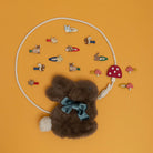 Plush mouse toy with a bow tie surrounded by small decorative items on an orange background