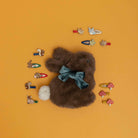 Brown teddy bear with a blue bow surrounded by various hair clips on an orange background