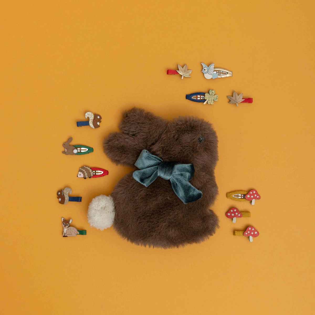 Brown teddy bear with a blue bow surrounded by various hair clips on an orange background
