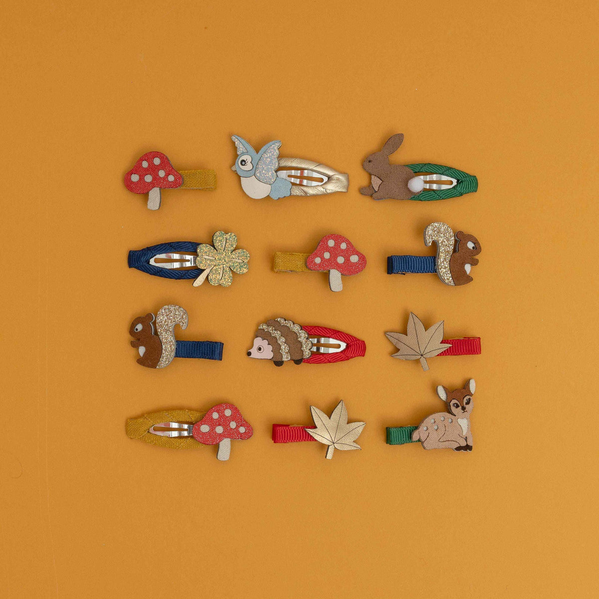 Nine colorful wooden hair clips shaped like nature elements including mushrooms, a squirrel, a hedgehog, a leaf, and a deer, arranged in a grid on a solid orange background.
