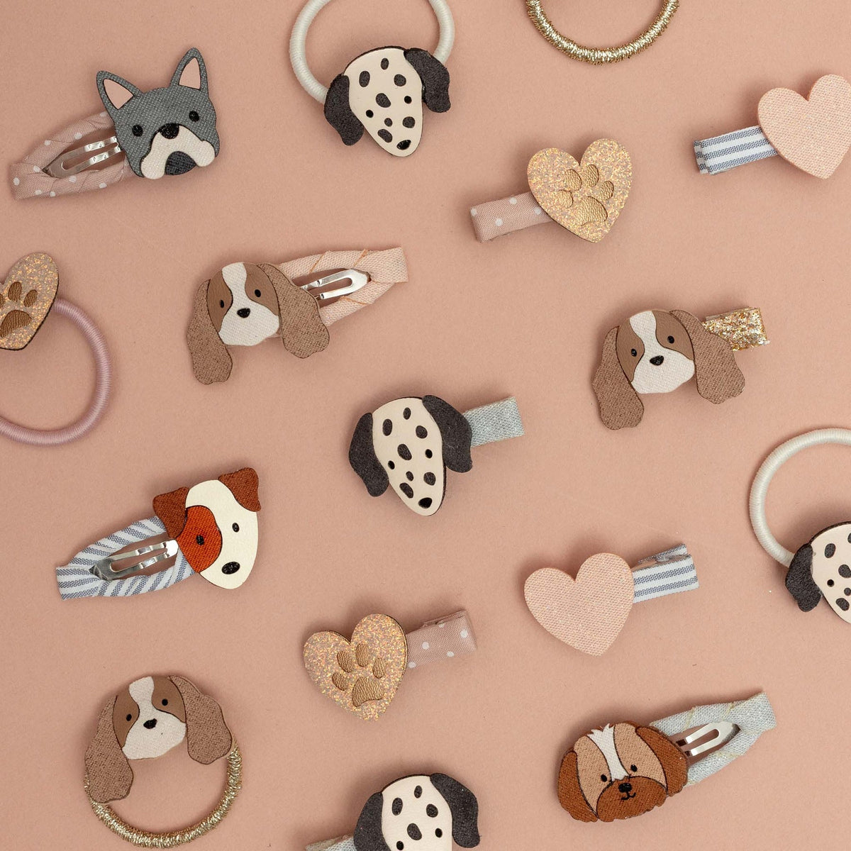 A styled flat-lay of various dog-themed hair clips and hair accessories arranged on a solid dusty pink background.
