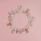 A circular arrangement of pastel hair clips featuring unicorn, bow, star, and rainbow designs on a solid pink background.
