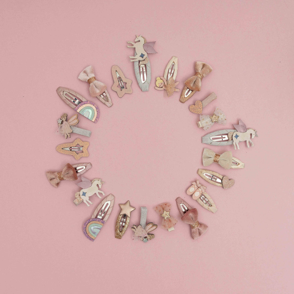 A circular arrangement of pastel hair clips featuring unicorn, bow, star, and rainbow designs on a solid pink background.