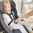 Child in a car seat with a hand adjusting a label on the harness.