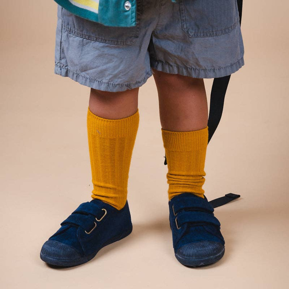 Person wearing mustard yellow knee-high socks and blue shoes on a beige background