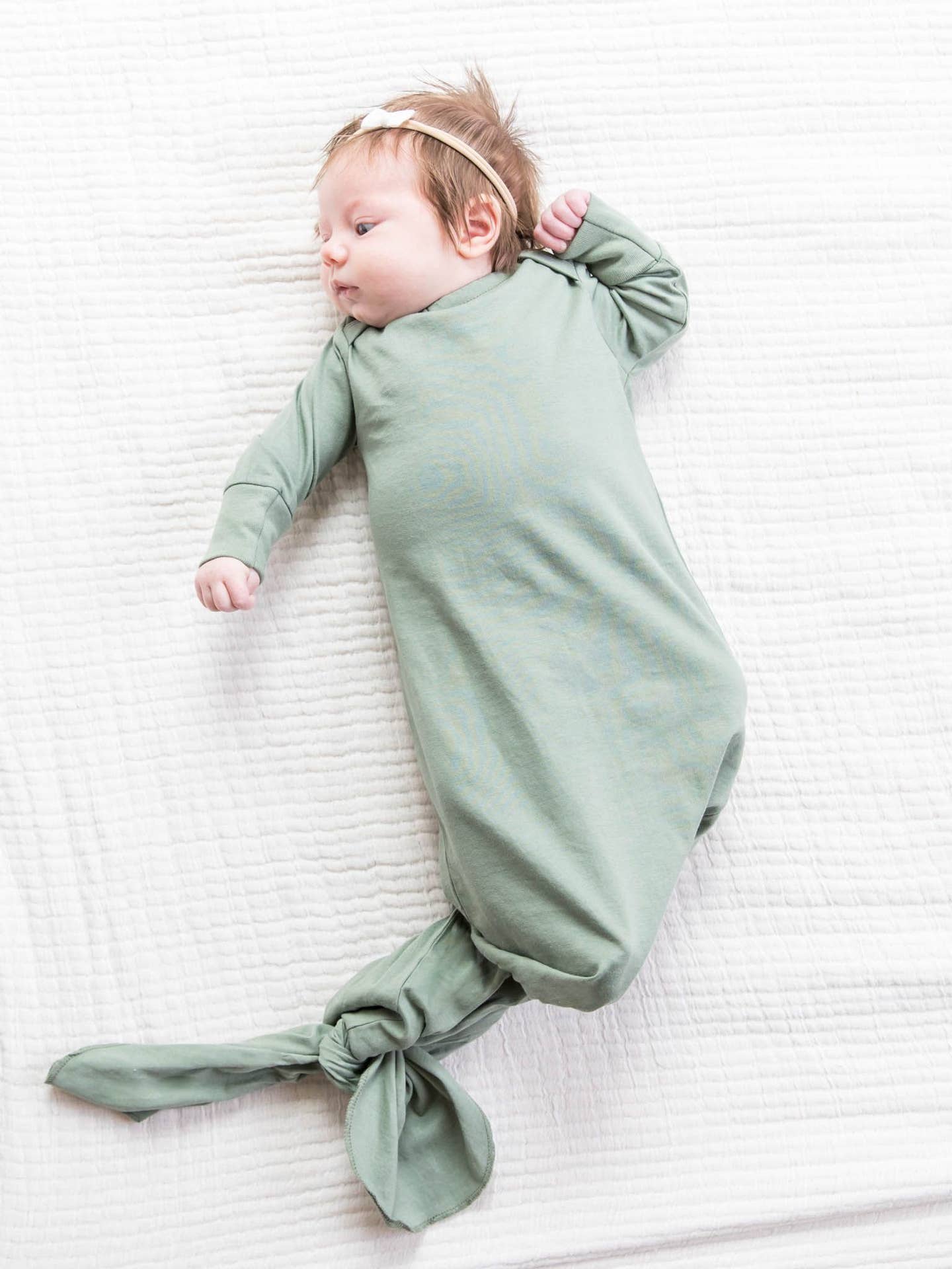Baby wrapped in a green swaddle on a white textured surface