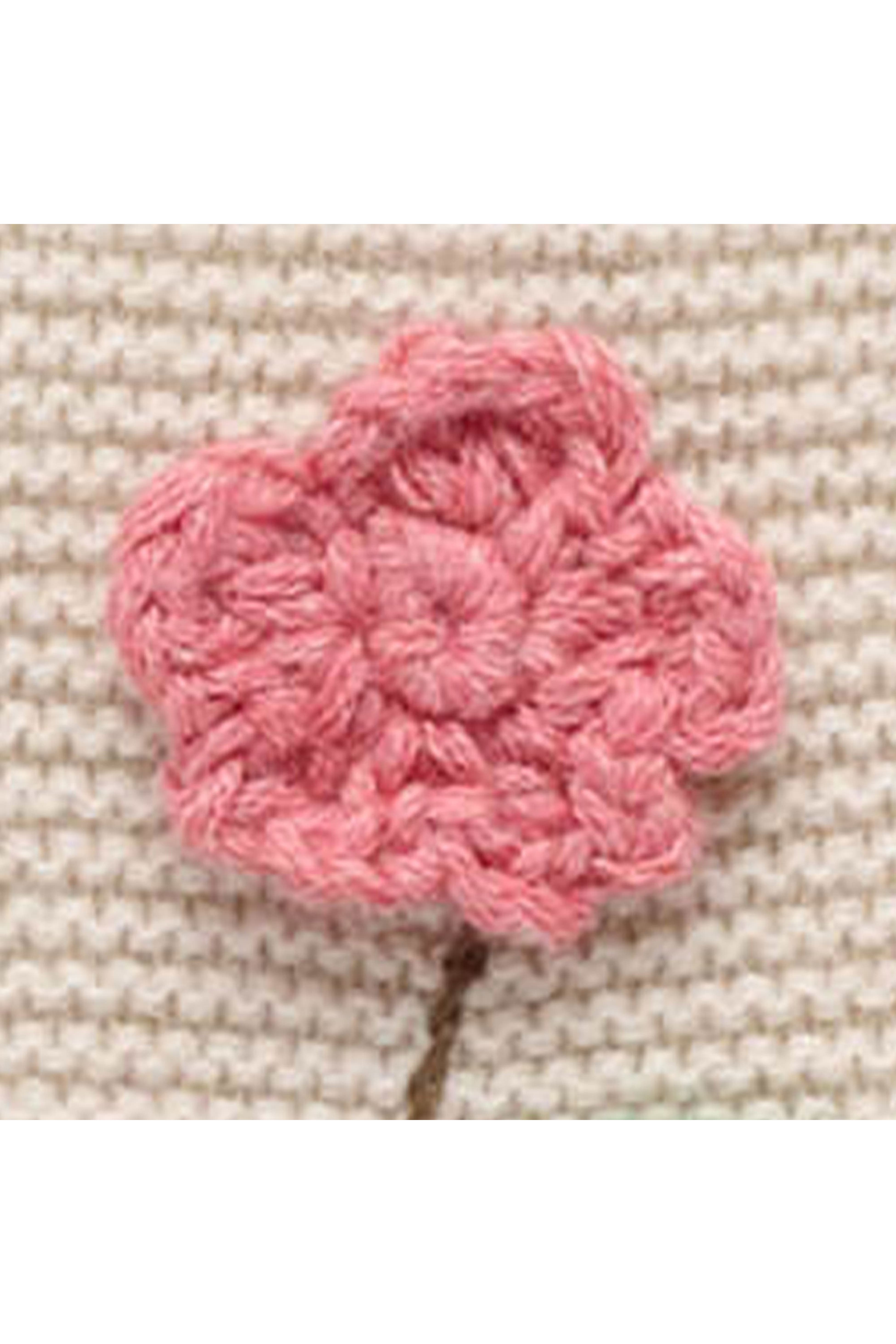A pink crocheted flower applique with a small brown stem, shown on a textured beige knit fabric background.