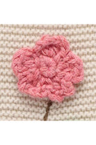 A pink crocheted flower applique with a small brown stem, shown on a textured beige knit fabric background.