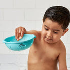 Child playing with a blue bath toy in a bathroom setting