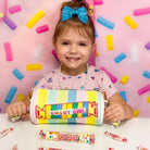 Child holding a colorful pencil case with 'Smart Girl' text against a pink background with candy decorations.