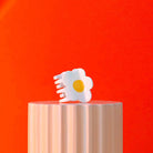 White flower-shaped object on a wooden block against a red background