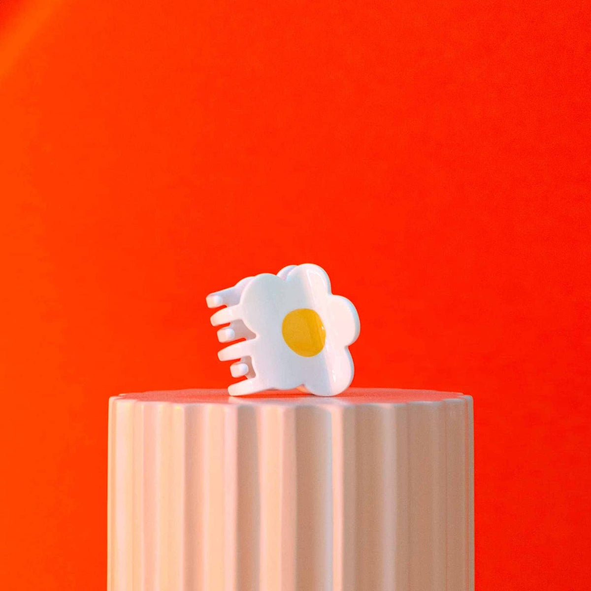 White flower-shaped object on a wooden block against a red background