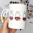 White mug with cartoon rabbit designs held against a colorful background