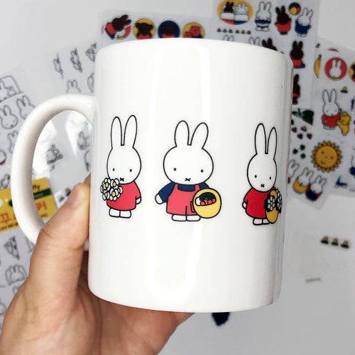 White mug with cartoon rabbit designs held against a colorful background