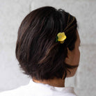 Person with a yellow hair accessory in their dark hair against a neutral background