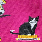 A close-up of a bright pink knit fabric featuring a black-and-white cat sitting on a yellow and white striped base.
