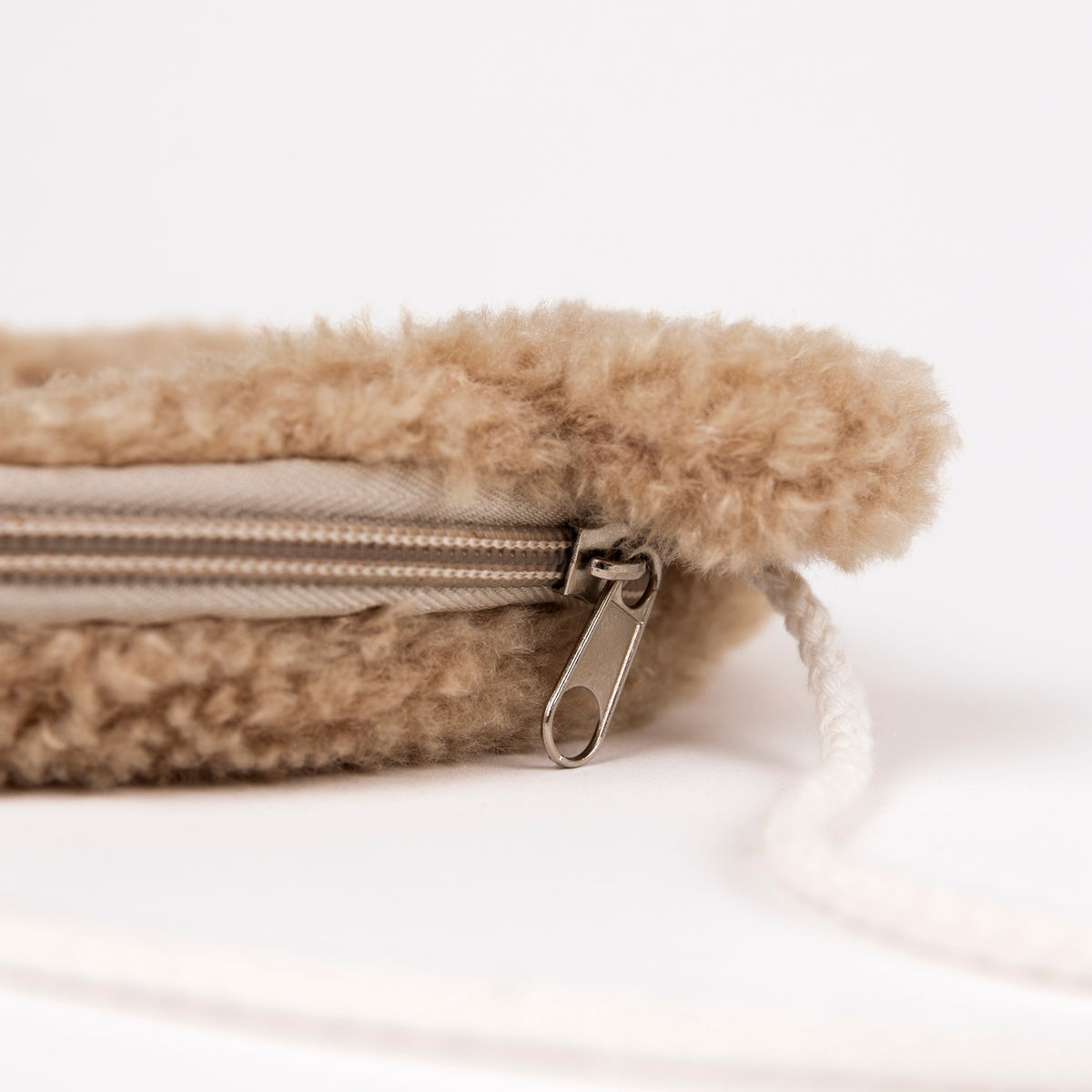 Close-up of a beige fuzzy fleece zippered pouch with a silver metal zipper pull and white drawstring cord on a white background.