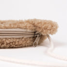 Close-up of a beige fuzzy fleece zippered pouch with a silver metal zipper pull and white drawstring cord on a white background.