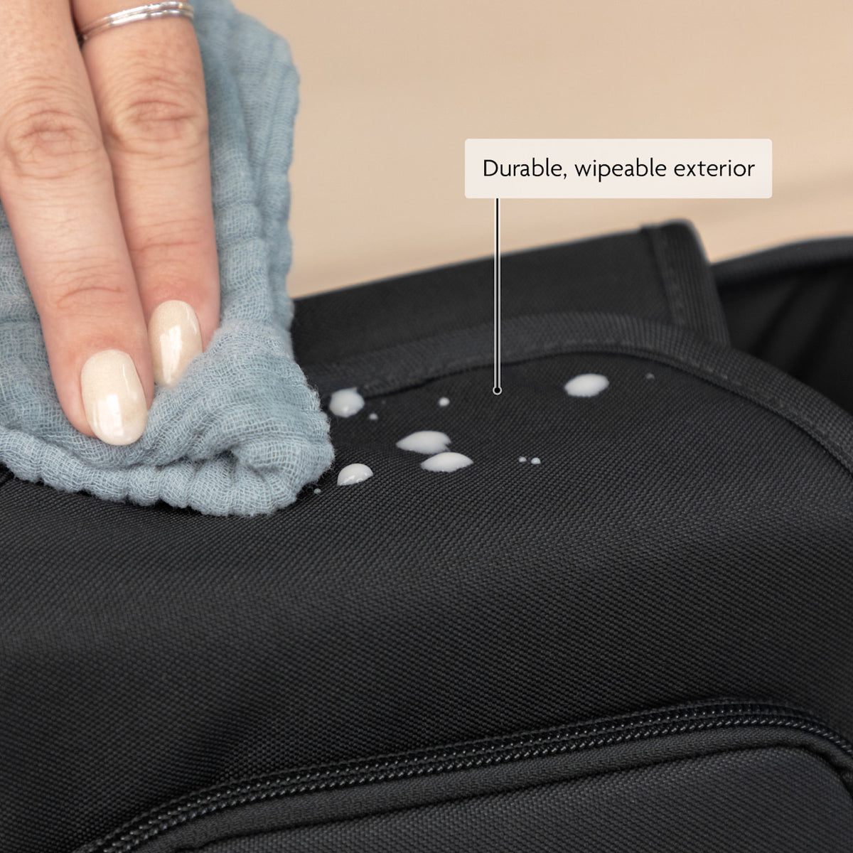 Person cleaning a black bag with a cloth, highlighting durable, wipeable exterior.