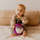 Baby sitting on a couch holding a purple toy