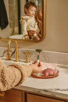 Person washing hands with soap in a bathroom, child reflected in mirror