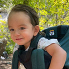 Child in a green baby carrier with a forest background