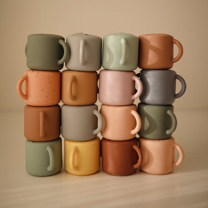 Stack of colorful ceramic mugs on a beige background