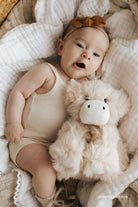 Baby lying on a soft surface with a plush toy, wearing a headband.