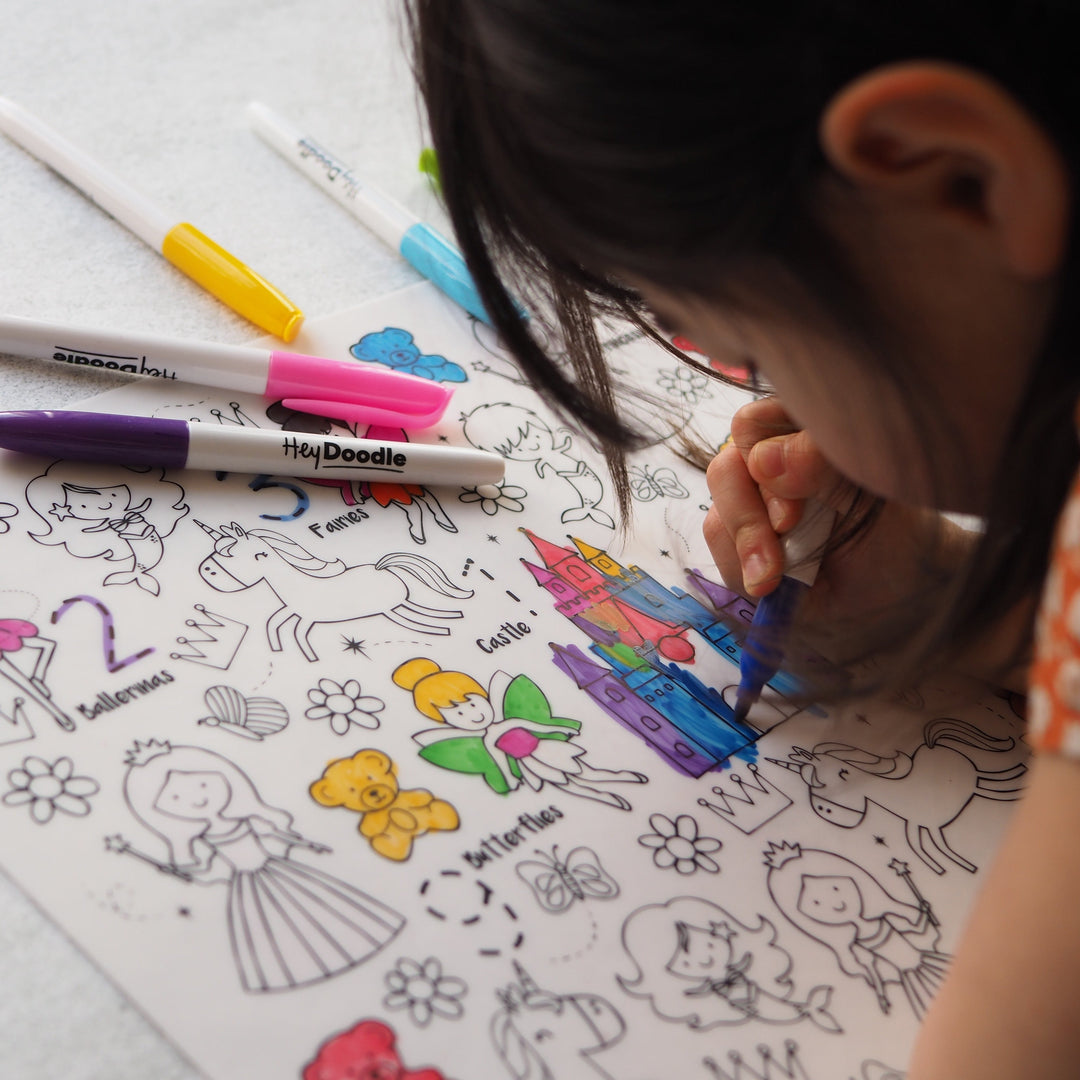 Child coloring a coloring book with markers on a white surface