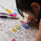 Child coloring a coloring book with markers on a white surface