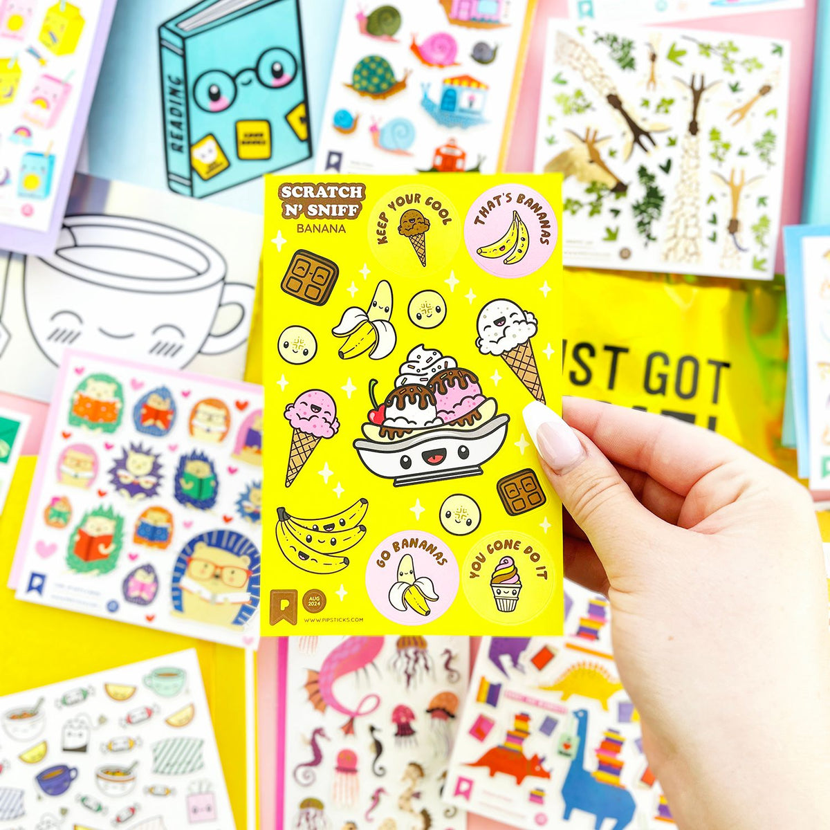 Hand holding a yellow scratch and sniff sticker book with various stickers on a colorful background