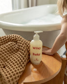 Wiley Baby bottle on a wooden stool next to a bathtub with a child's hand reaching out.