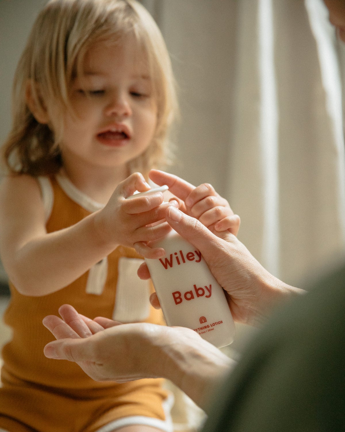 Child holding a bottle labeled 'Wiley Baby' with an adult's hand.