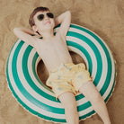 Child lying on a green and white striped pool float in the sand
