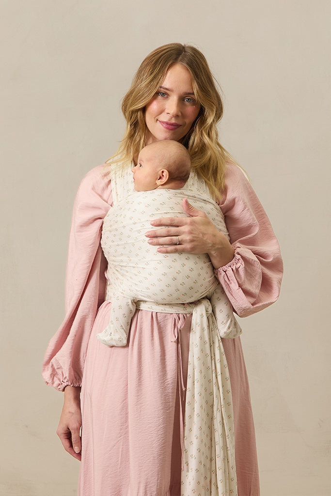 Woman holding a baby wrapped in a white wrap against a beige background