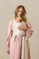 Woman holding a baby wrapped in a white wrap against a beige background