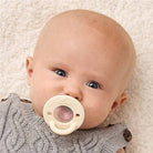 Baby wearing a beige pacifier on a soft beige background
