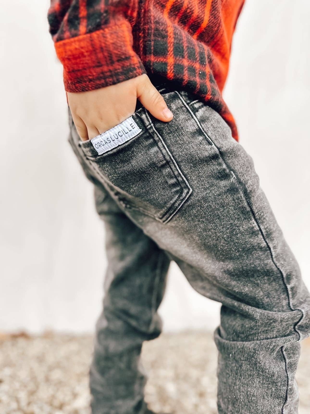 Person wearing gray jeans with a visible brand label, standing on a gravel surface.