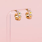 Gold hoop earrings with daisy flowers on a pink background