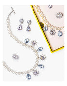 A pearl jewelry set arranged on a white background, including a necklace with teardrop and flower-shaped blue crystal accents, matching earrings, and a partial matching necklace displayed inside a pink box with a yellow border.