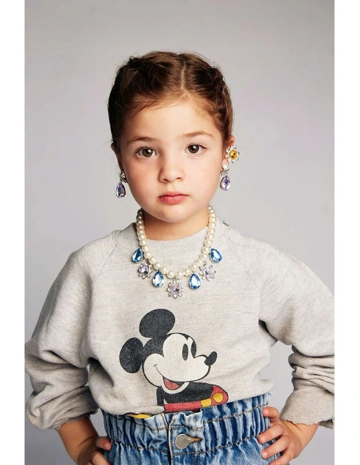 Child wearing colorful earrings and jewelry against a purple background